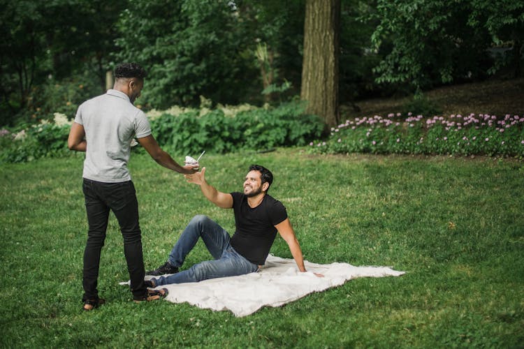 Photo Of A Man In A Gray Shirt Giving Food To A Man In A Black Shirt