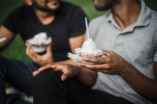 Men Sitting Next to Each Other while Holding Cups of Ice Cream