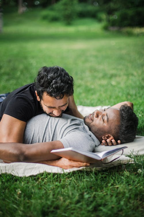 Men Resting on a Picnic Blanket while Holding a Book