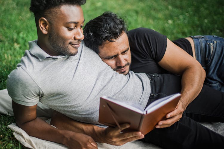 Two Adult Men Lying Together And Reading Book