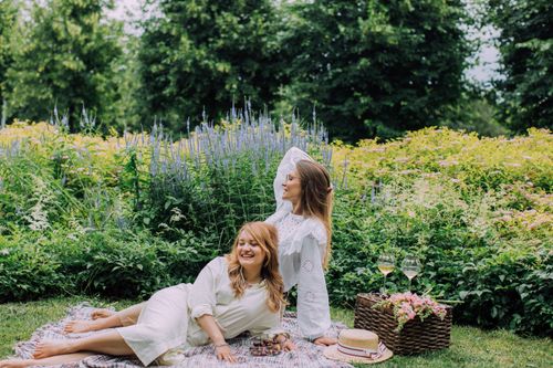 Free Two women enjoying a sunny picnic in a vibrant summer garden with wine and flowers. Stock Photo