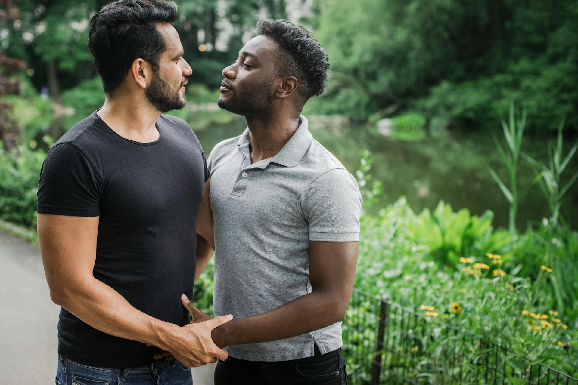 Two men embracing near a pond in a public park, sharing a moment of romance and connection.