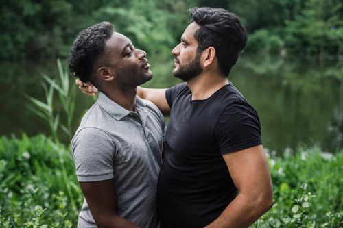 Free Interracial couple embracing outdoors by a serene lake, depicting love and unity. Stock Photo