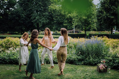 Women Holding Hands while Dancing Barefoot at a Park