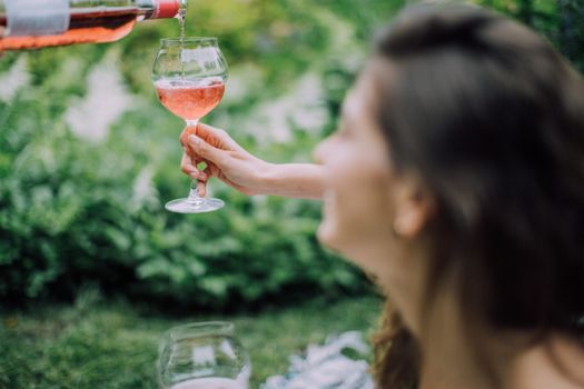 阳光明媚的户外野餐中，一名女子优雅地将玫瑰葡萄酒倒入玻璃杯，轻松捕捉到夏日的氛围