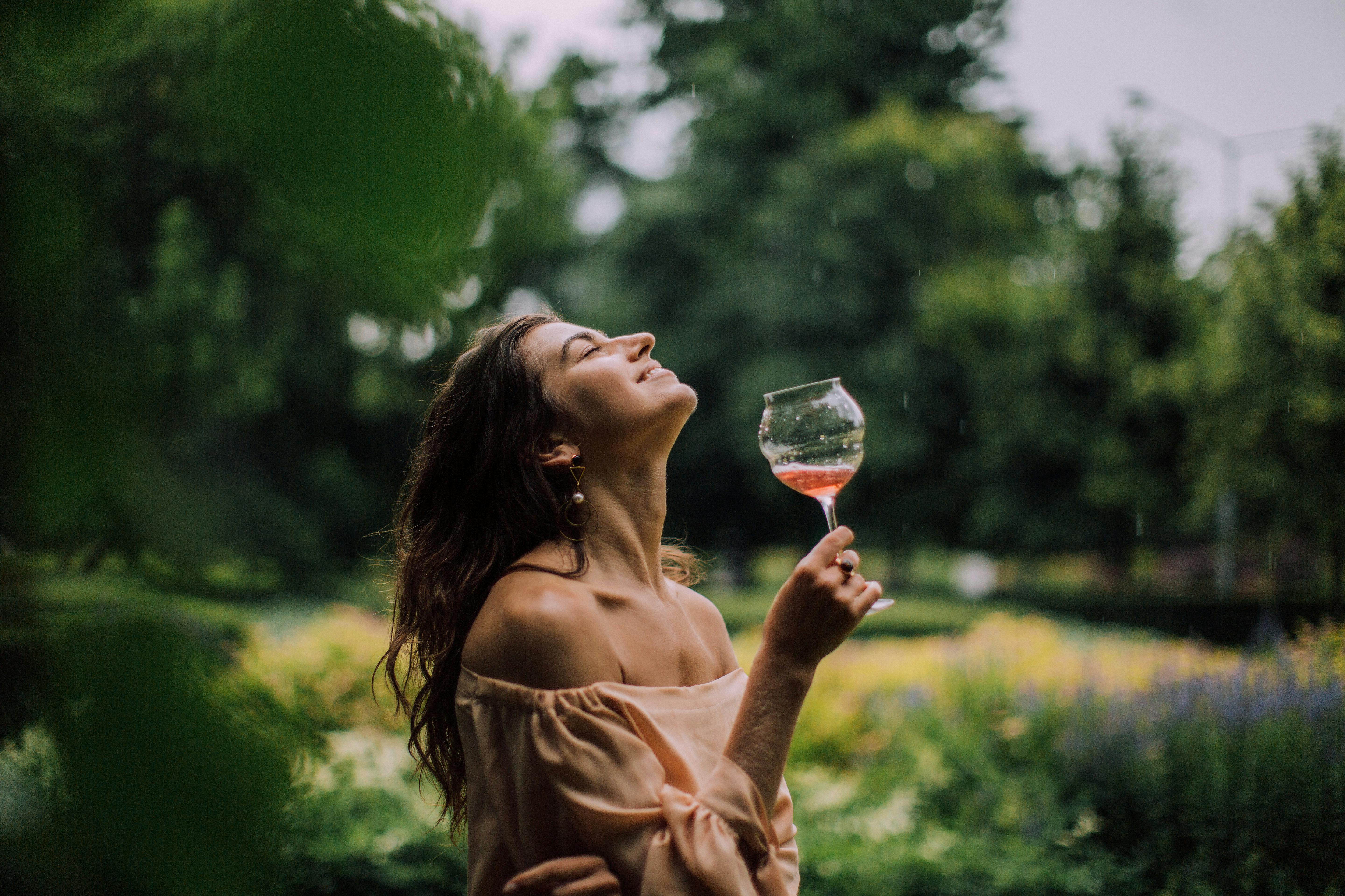 一位快乐的女子在户外，一边品味着葡萄酒，一边享受着雨中的惬意时光
