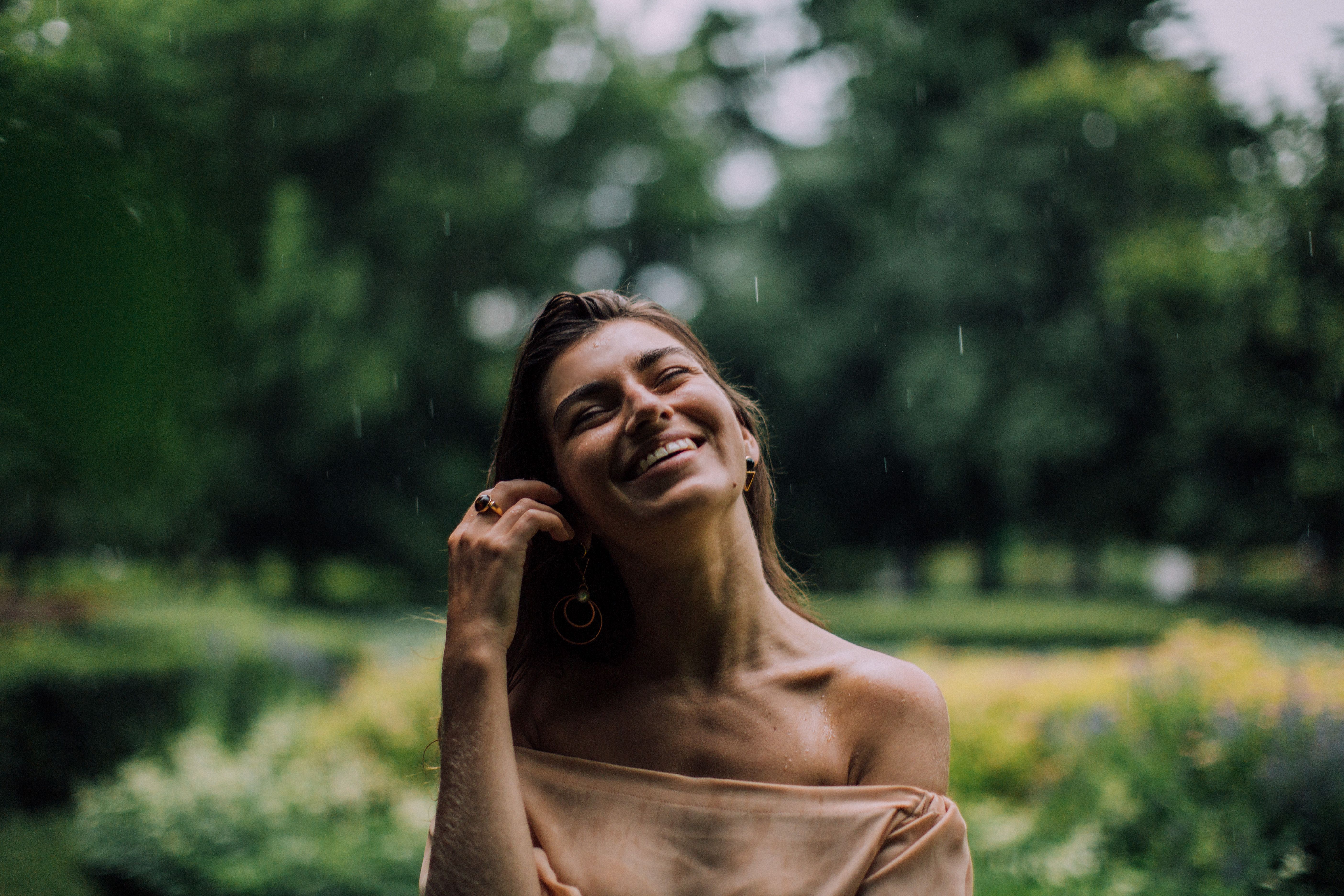 一位面带微笑的女子在绿意盎然的公园里享受着雨水的滋润，洋溢着幸福与宁静
