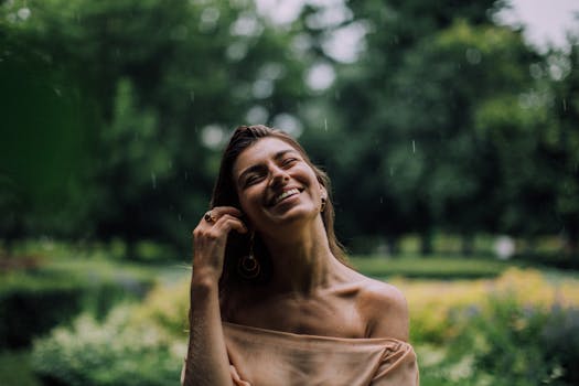 A smiling woman enjoying the rain in a lush green park, exuding happiness and tranquility.