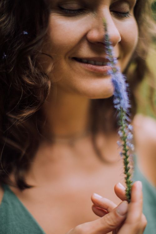 Free A serene close-up of a woman smiling with eyes closed, holding a lavender flower outdoors. Stock Photo