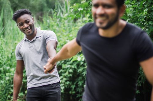 Free Two men happily hold hands outdoors, surrounded by greenery. Stock Photo