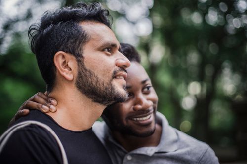 Free Two men smiling and embracing outdoors with a beautiful blurred bokeh background. Stock Photo