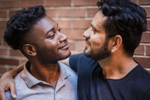 Free Two men smiling and embracing affectionately against a brick wall backdrop. Stock Photo