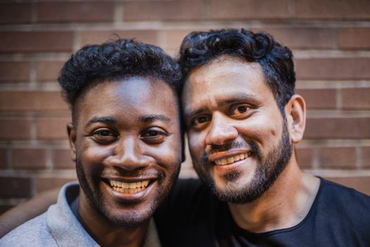 Close-up portrait of two happy friends smiling together against a brick wall.