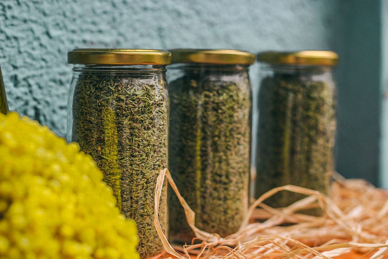Several glass jars of dried herbs lined up against a textured wall