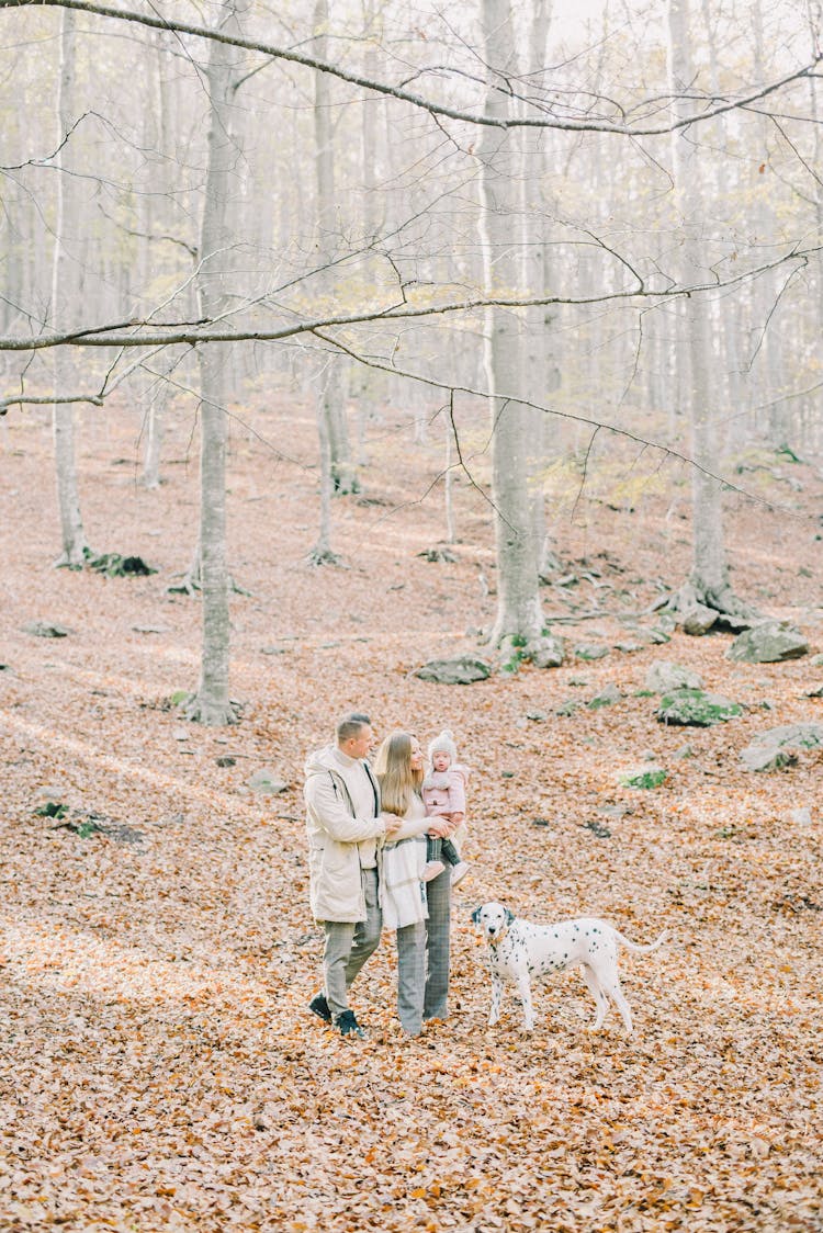 A Happy Family Standing In The Woods With A Dog