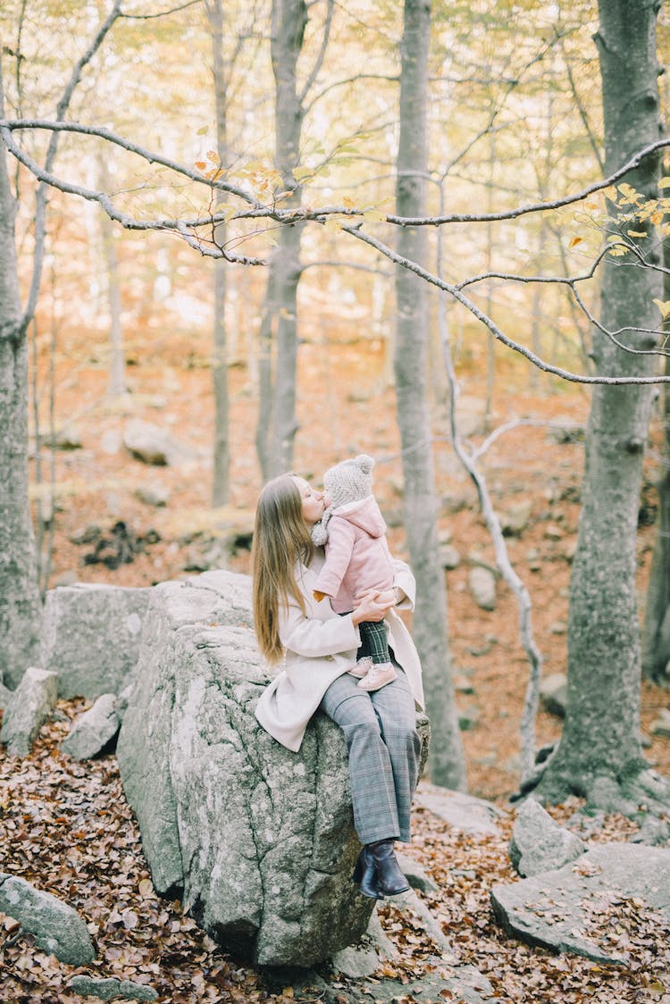 Woman Sitting On Gray Rock Kissing Her Baby