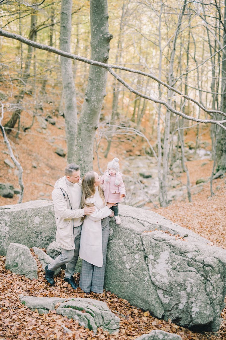 A Man And A Woman Standing Beside A Rock With A Baby