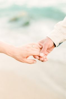 海滩上，两个人手牵手的特写象征着爱与亲密