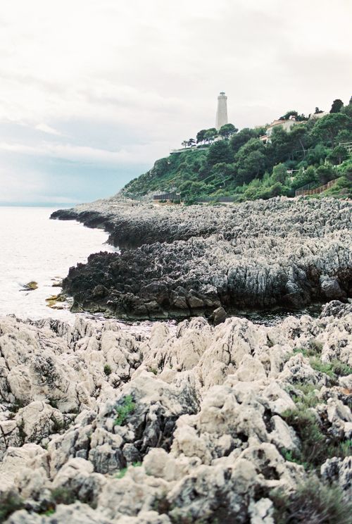 Free Dramatic rocky coast featuring a lighthouse and lush greenery under cloudy skies. Stock Photo