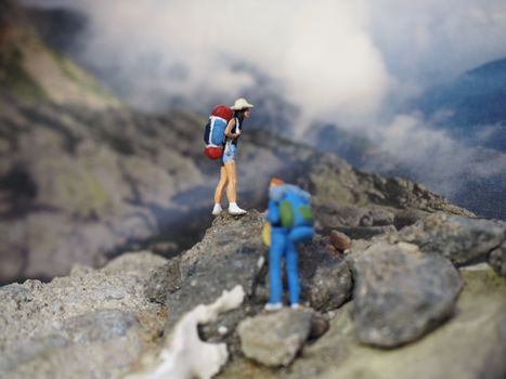 Close-up of miniature hiking figurines placed on rocky terrain with a blurred landscape background.