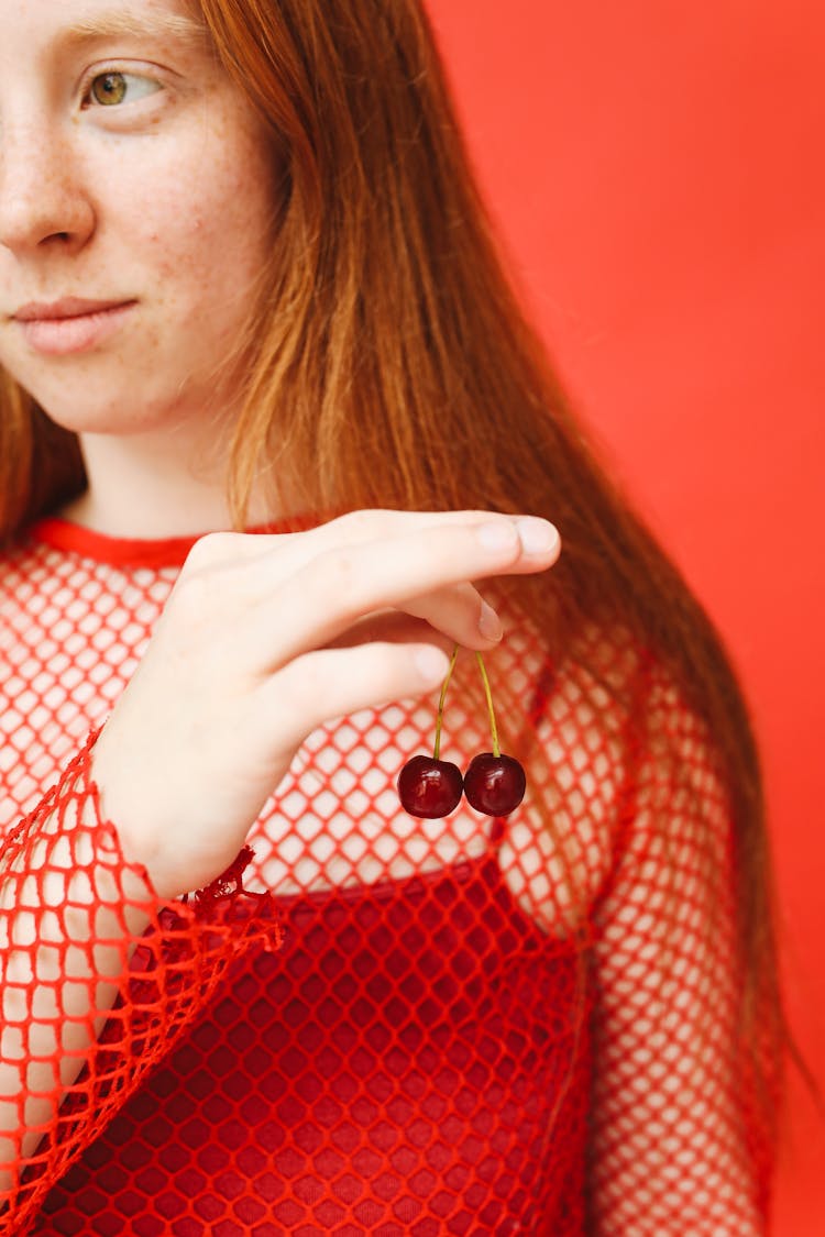 A Woman In A Red Outfit Holding Cherries