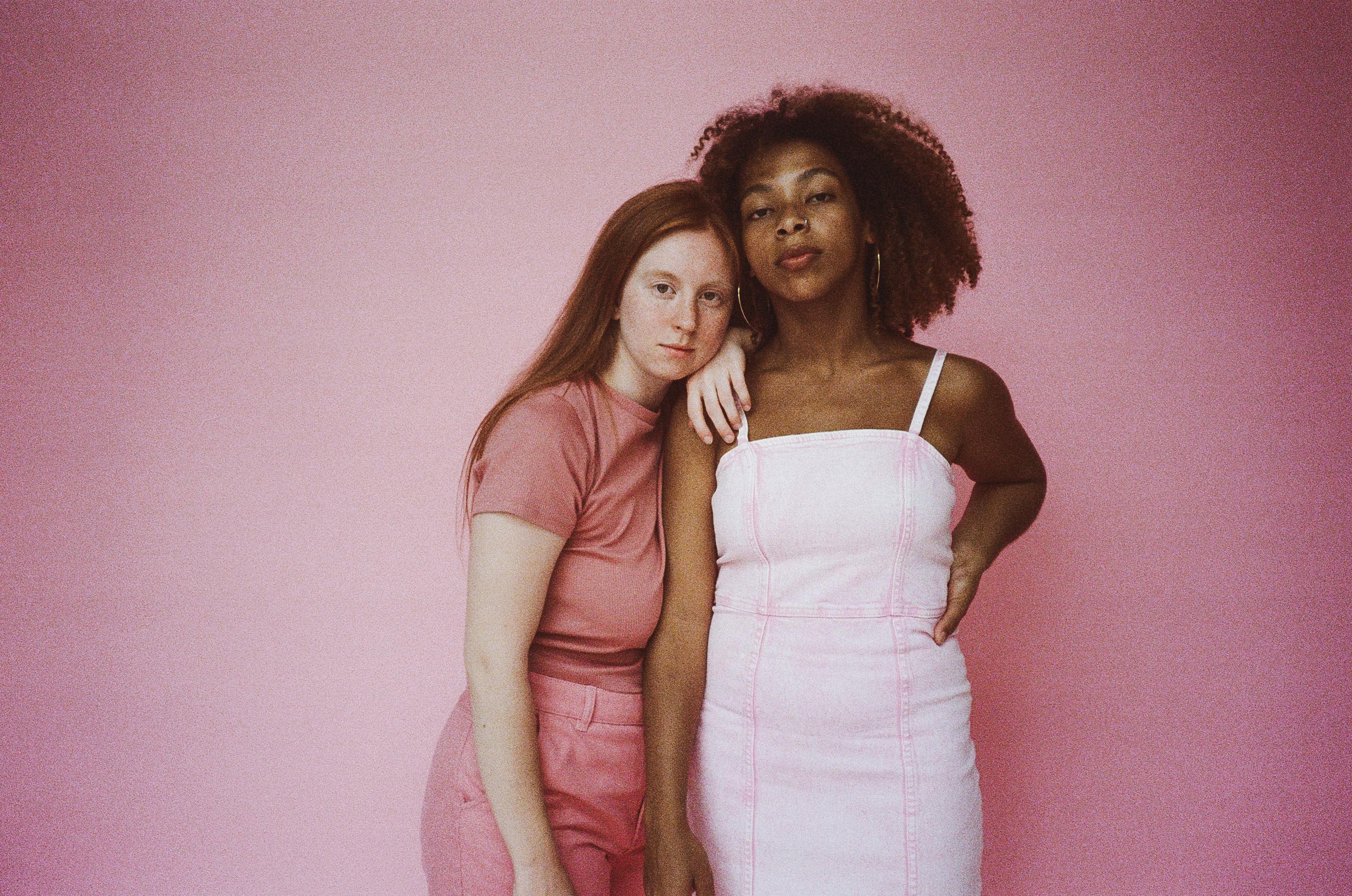 Fashionable portrait of two women posing in a pink studio background, highlighting style and friendship.