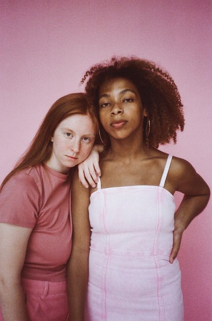 Stylish studio portrait featuring two diverse models posing against a pink background.