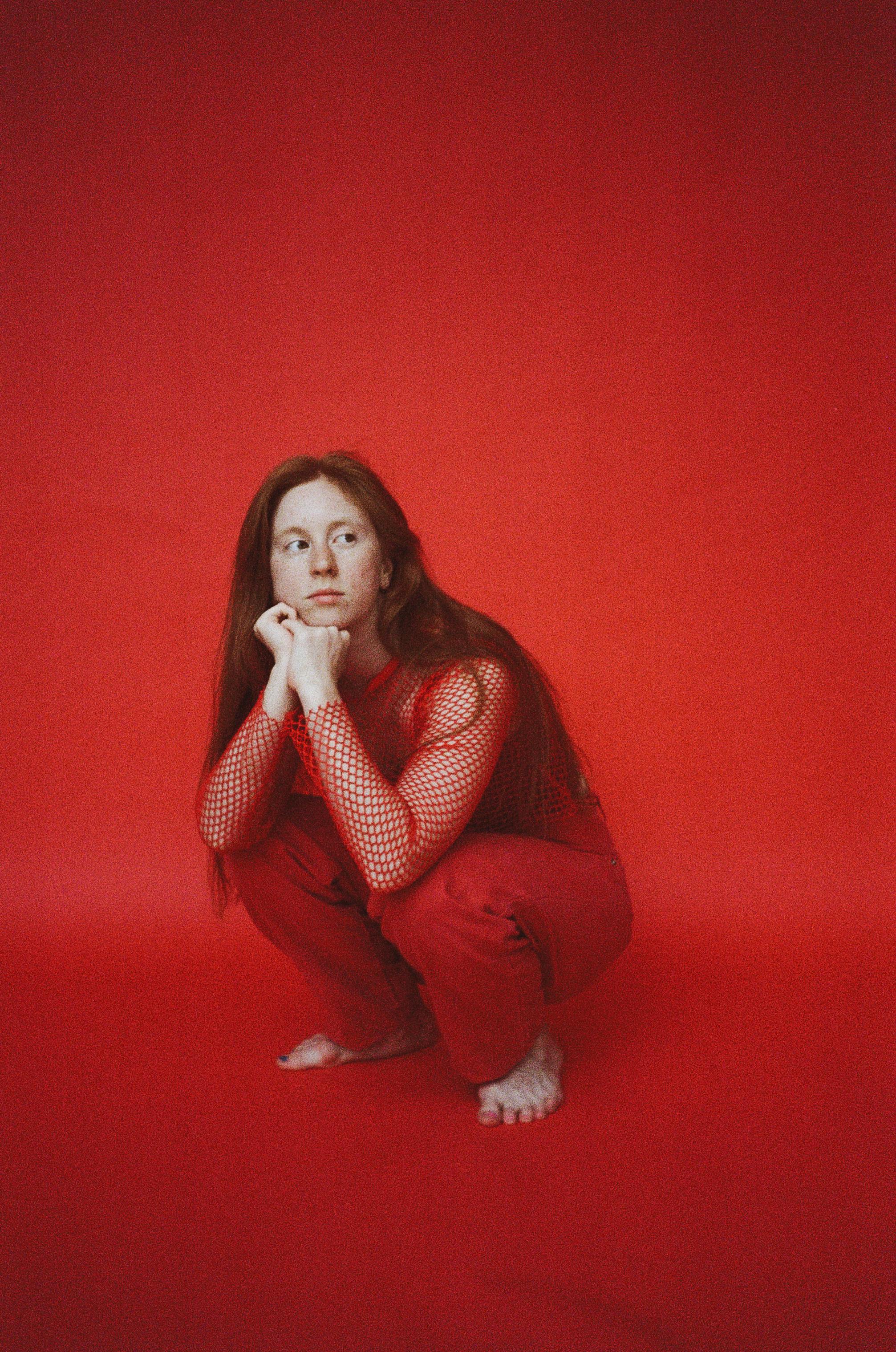 A woman in red clothing poses thoughtfully against a vibrant red background in a studio.