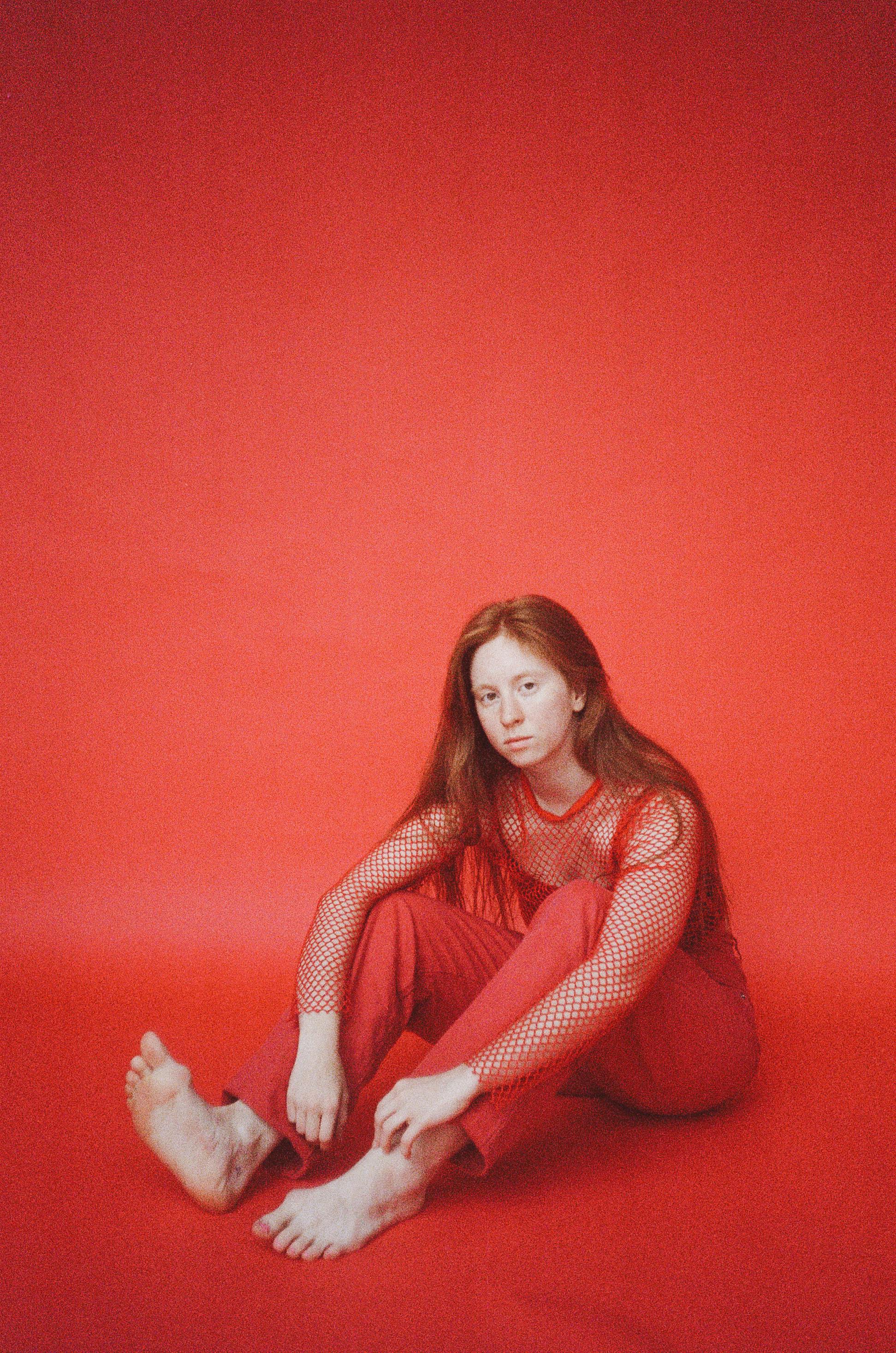 barefooted woman in red outfit sitting on red floor