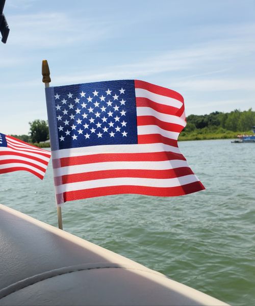 Free American flag waving on a boat by a lake under a clear blue sky. Stock Photo