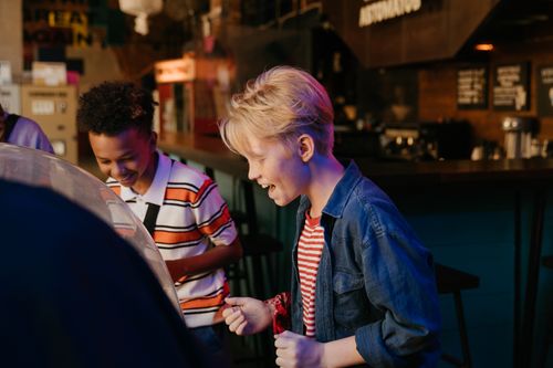Free Two teenagers having fun at an arcade, filled with laughter and excitement. Stock Photo