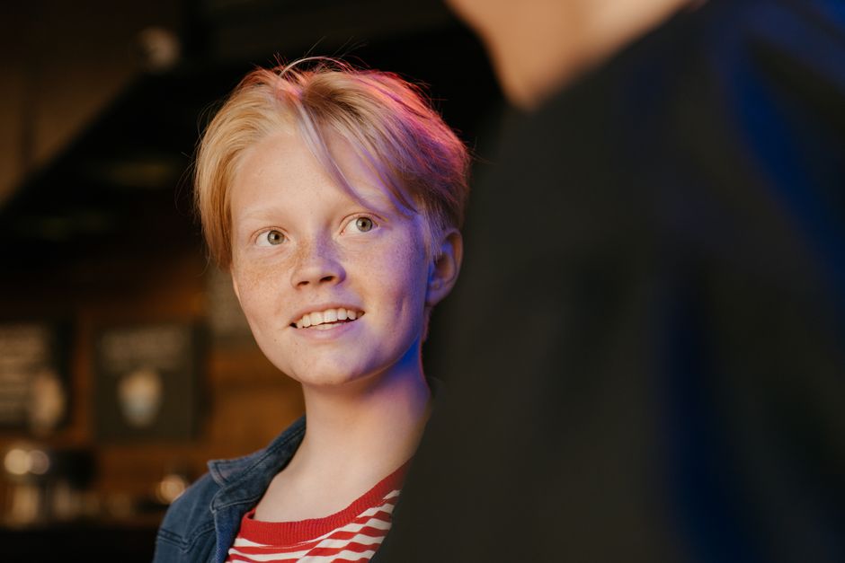 Smiling teen with freckles enjoys a casual indoor setting, radiating happiness.