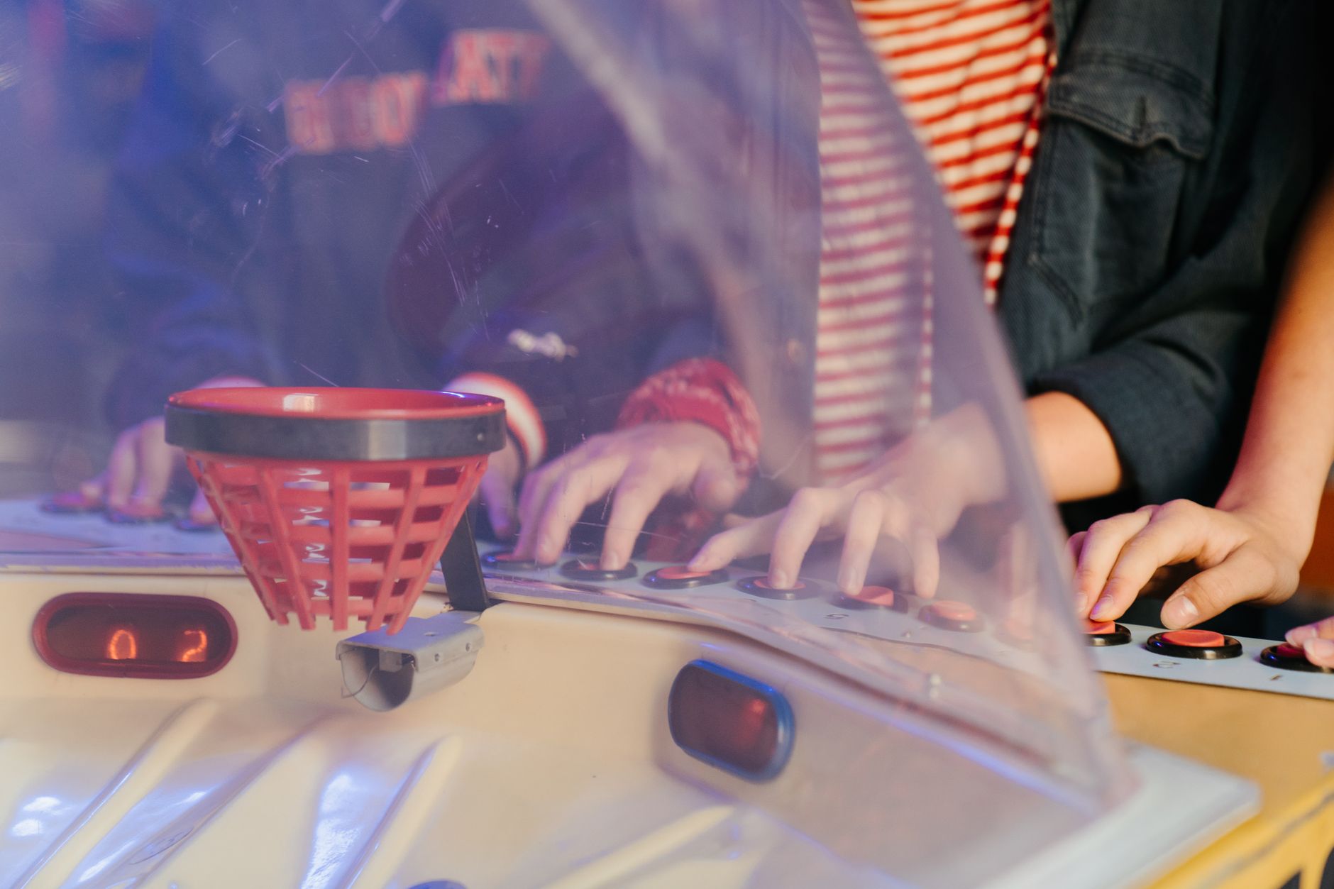 Friends enjoy a vintage arcade basketball game, highlighting retro nostalgia and playful fun.