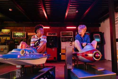 Free Two teenagers enjoying a playful moment on arcade rides in a vibrant amusement setting. Stock Photo