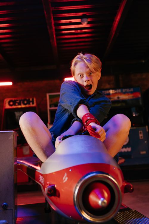 Free Blonde teenage boy having fun on a red ride at an amusement arcade. Stock Photo