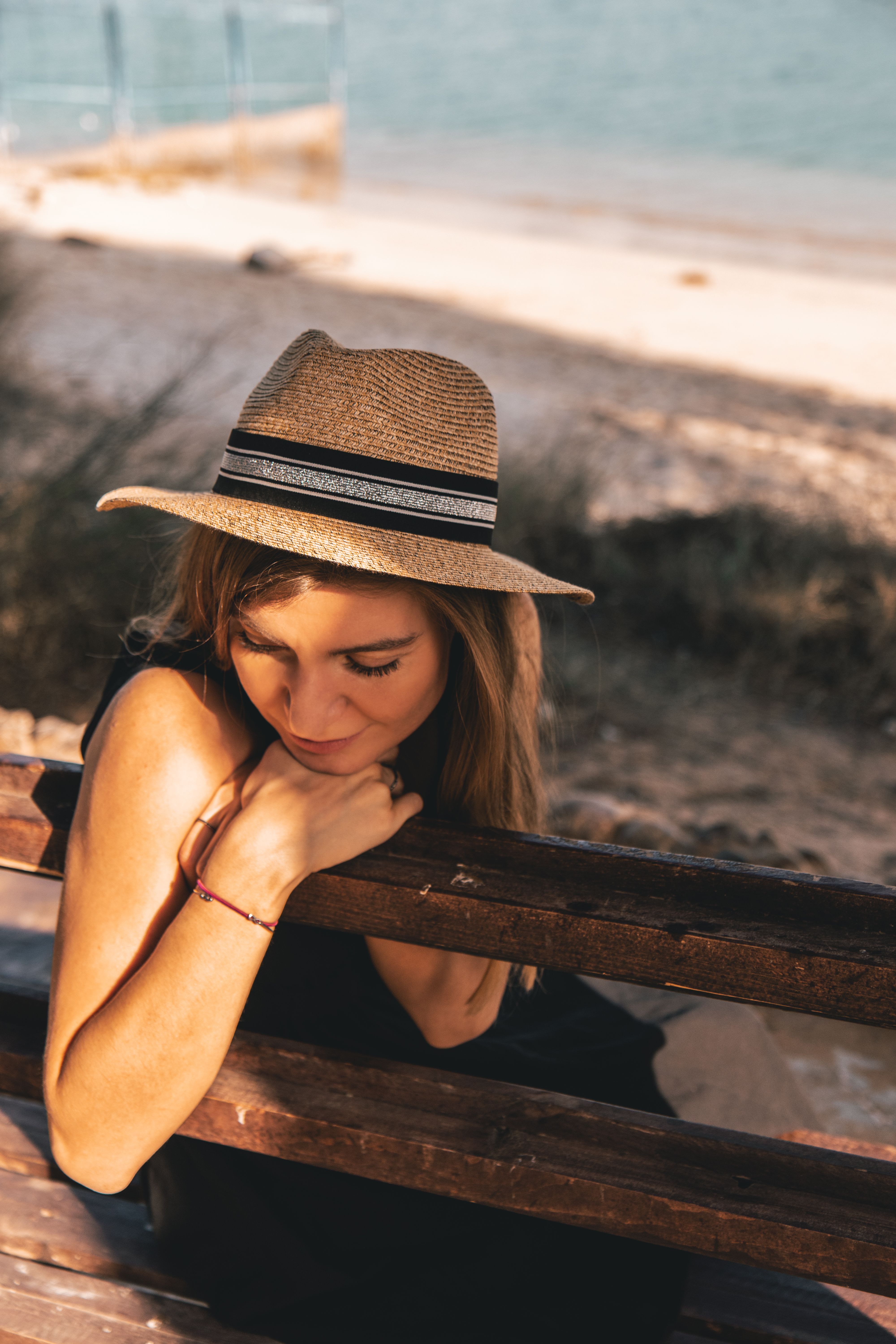Woman sitting on a beach bench in summer wearing a straw hat, relaxing under the sun.
