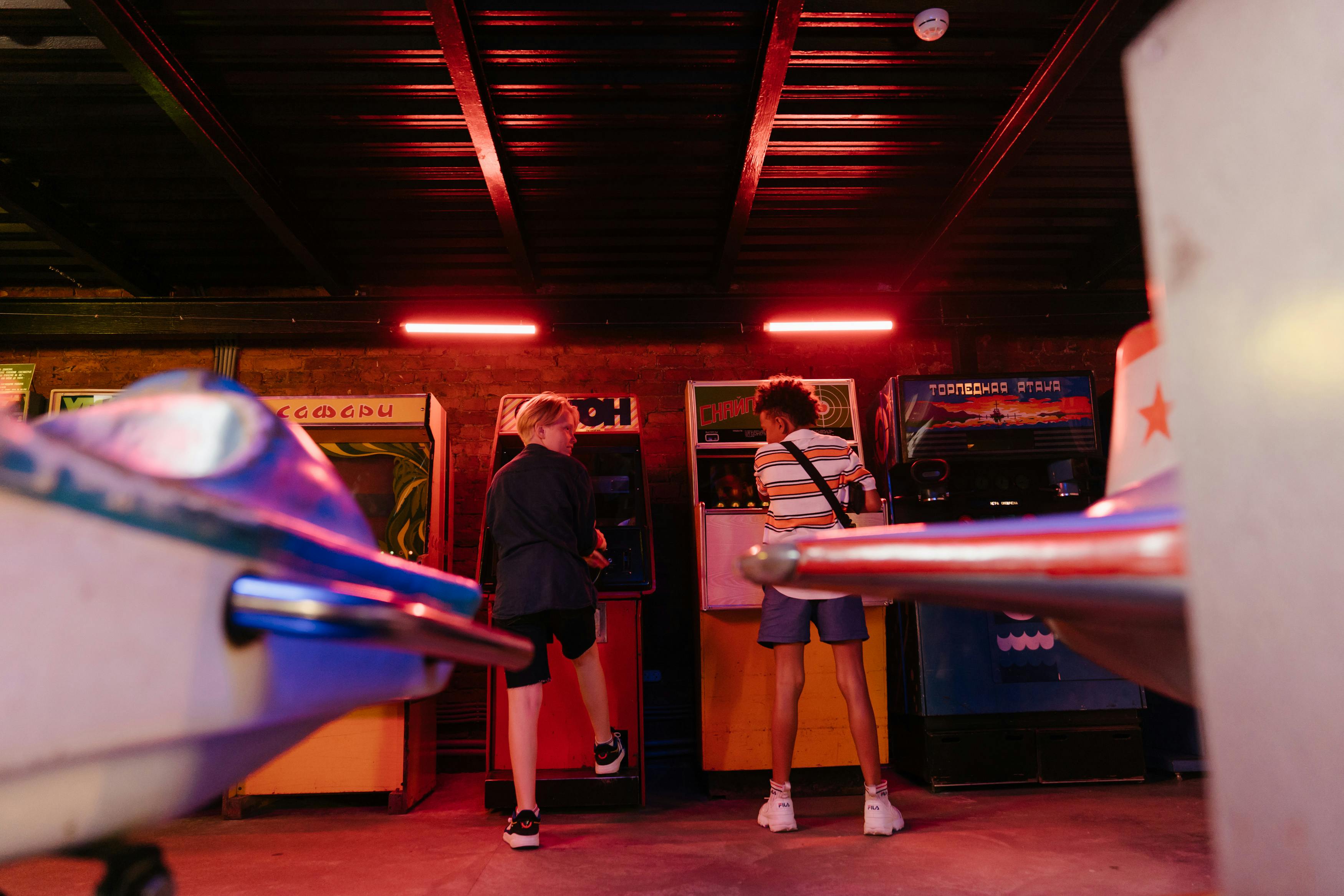 Teenagers playing classic arcade games in a dimly lit amusement arcade, embracing a retro vibe.