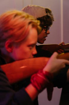 Two teenagers engage in a playful shooting game at an indoor arcade, showcasing teen spirit.