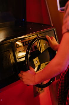 Hands on a vintage arcade driving game machine with a steering wheel and retro design.