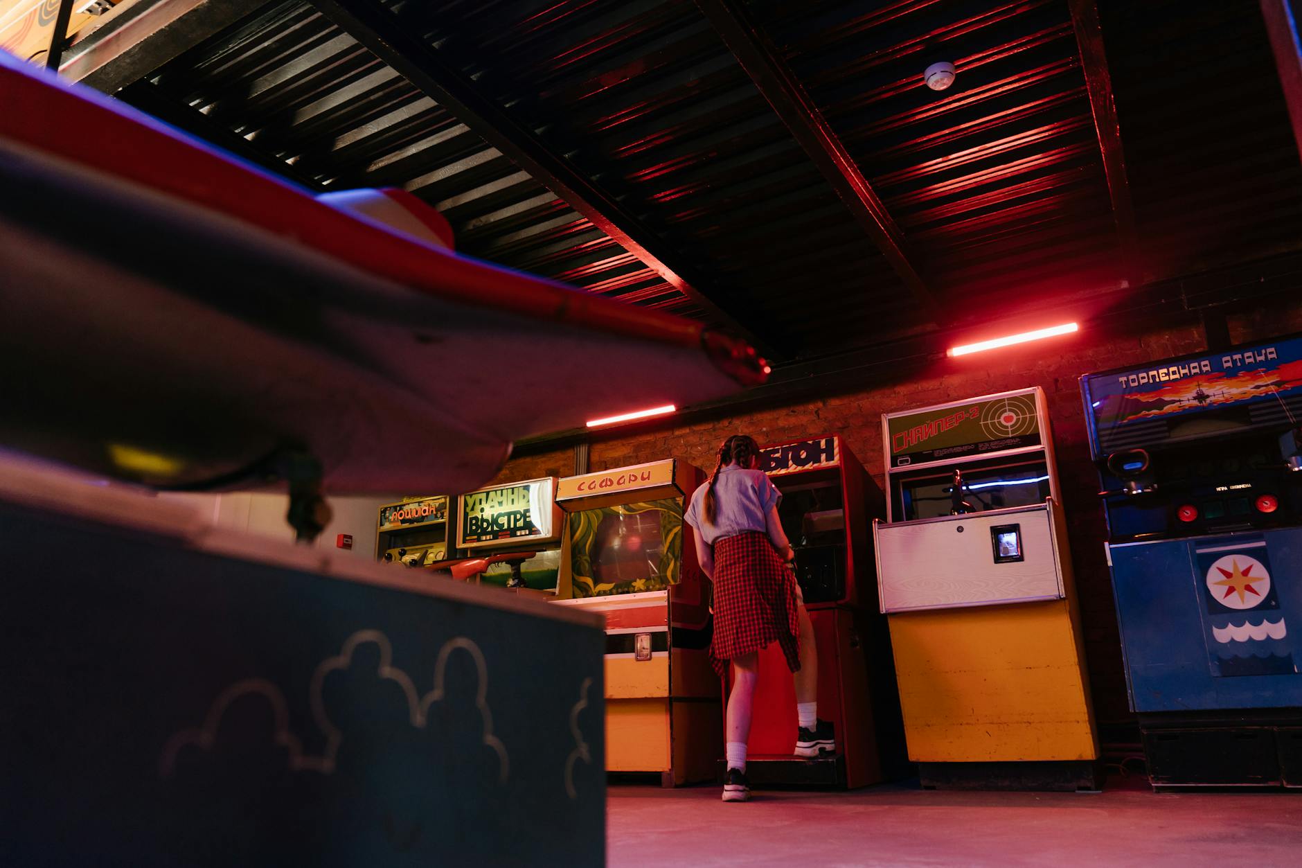 Teen girl enjoying retro arcade games in a dimly lit indoor amusement area.