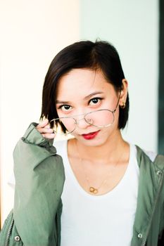 Portrait of a young Asian woman in eyeglasses, exuding confidence and style indoors.
