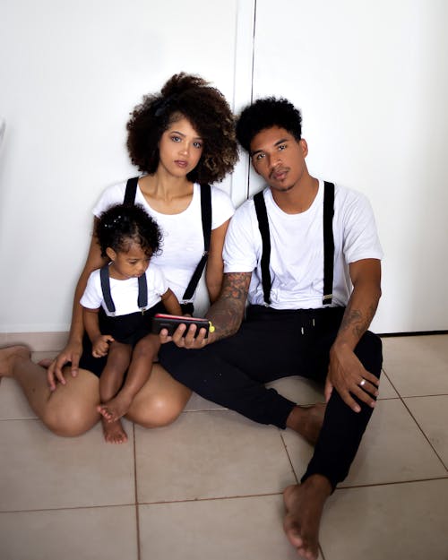 Black family in stylish outfits with daughter watching smartphone
