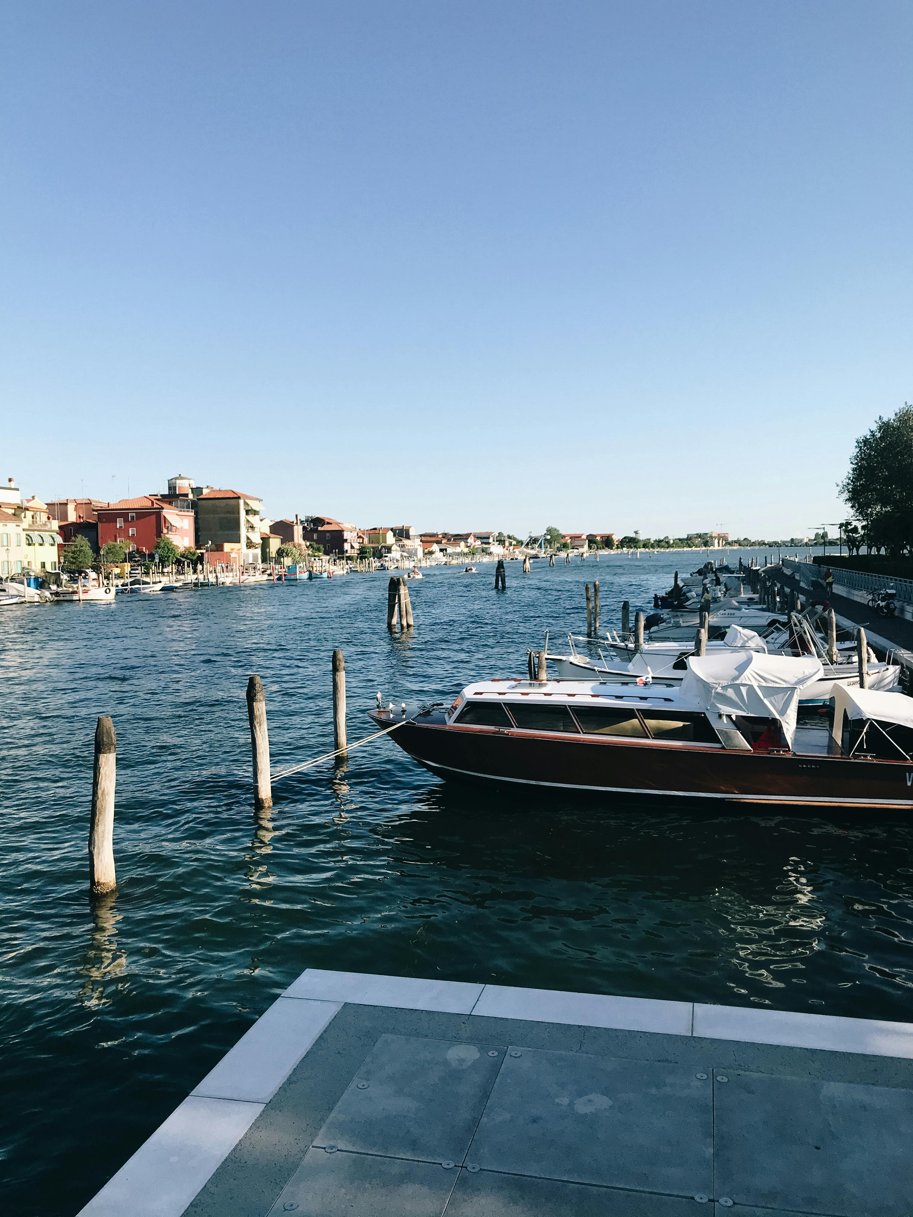 Free Calm canal with docked boats under a blue sky in Venice, Italy. Stock Photo