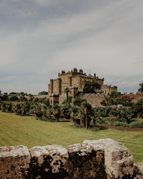 A picturesque view of Culzean Castle surrounded by lush greenery under a cloudy sky in Scotland.