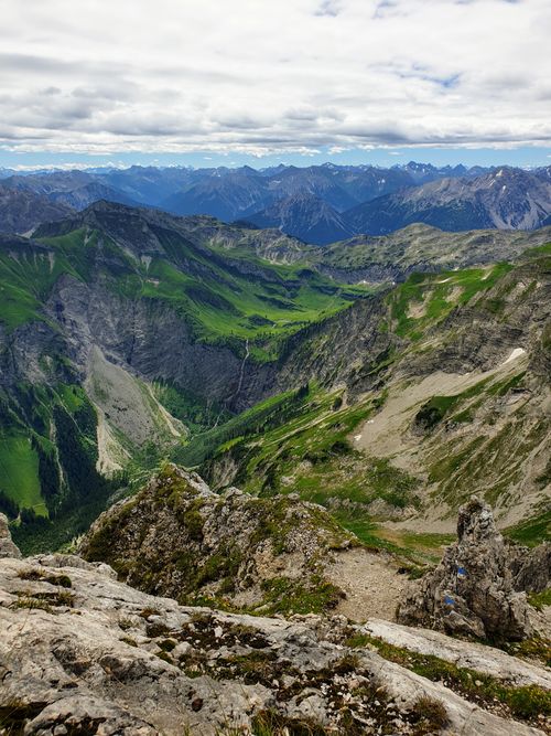 Free Stunning aerial view of vibrant green and rocky mountain terrain under a cloudy sky. Stock Photo