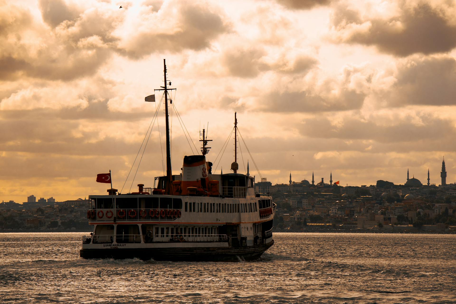 Ferry boat sailing on the Bosphorus during sunset in Istanbul with city skyline and dramatic clouds.