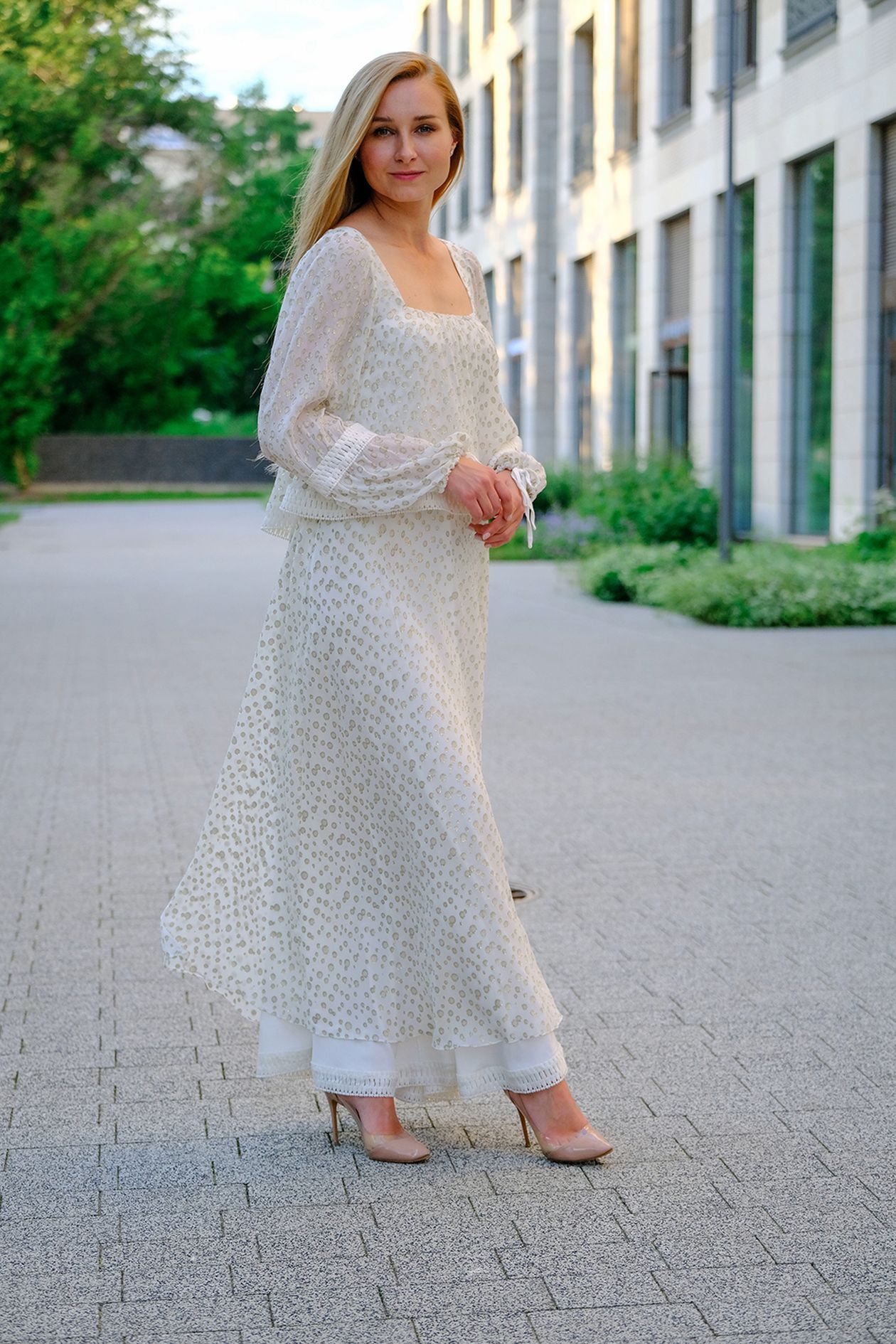 Woman in a white patterned long-sleeve maxi dress standing on a sidewalk