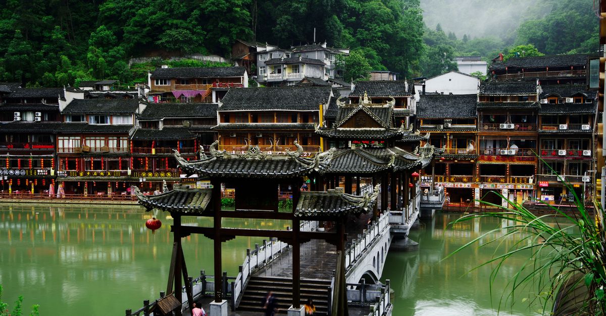 Explore the serene Fenghuang's historic bridge and riverside town under lush greenery.