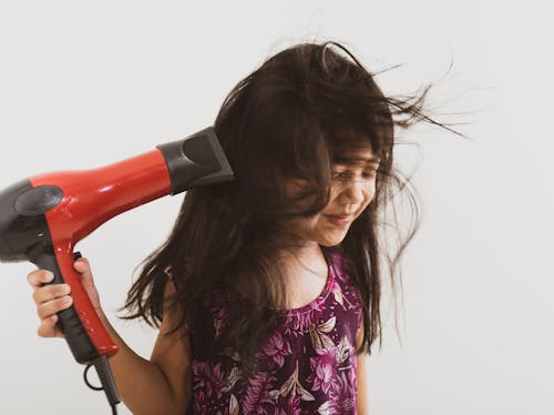 Close-Up Shot of a Girl in Floral Top Using a Hair Blower