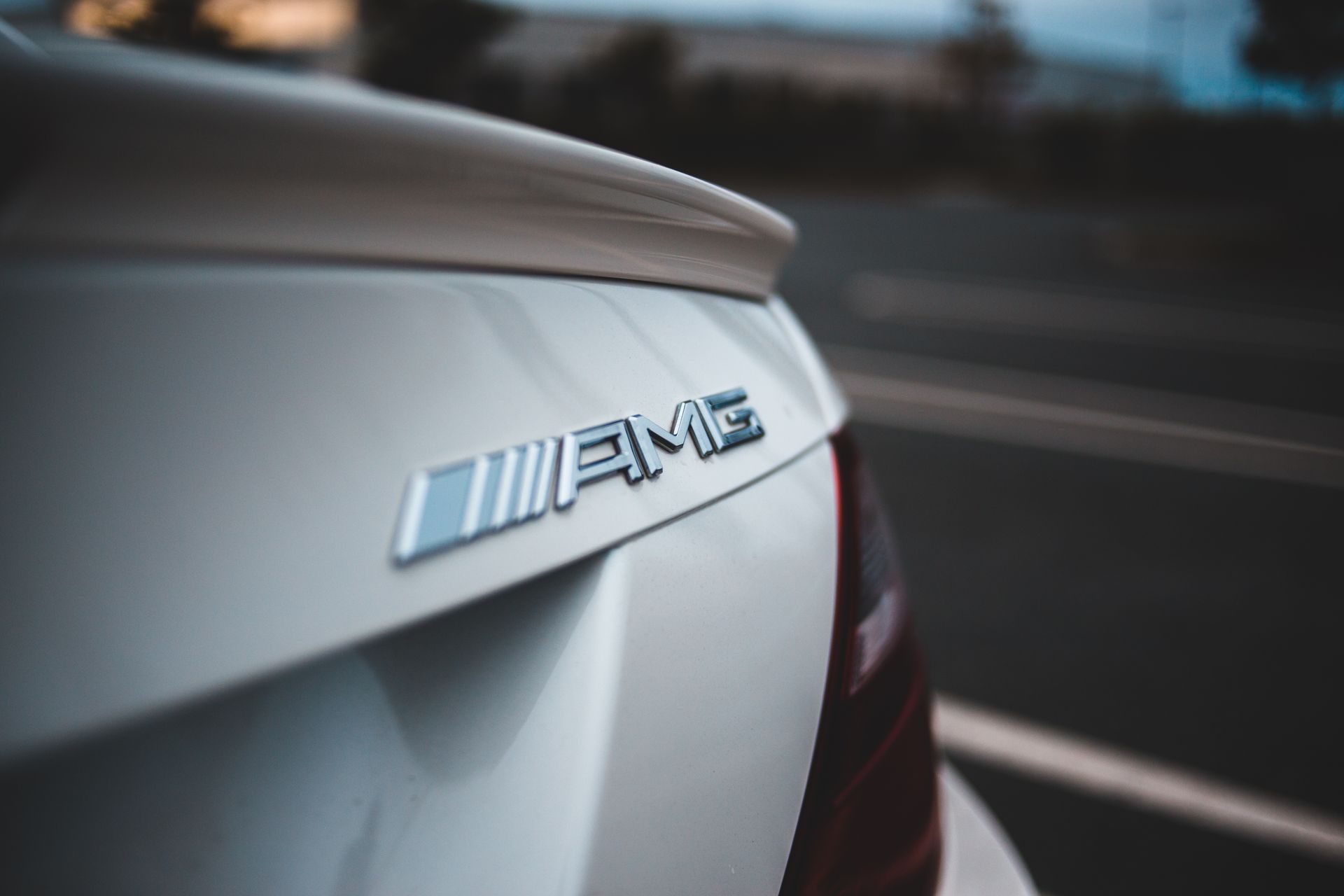 Closeup of chrome logotype on trunk of new shiny white modern car driving on asphalt road
